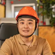 Un hombre con casco sonríe sentado a su mesa de trabajo.