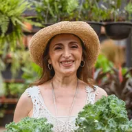 Una mujer con sombrero sostiene dos plantas en su vivero.